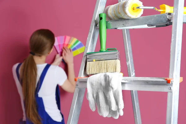 Escada com ferramentas de pintura e jovem decorador no fundo — Fotografia de Stock
