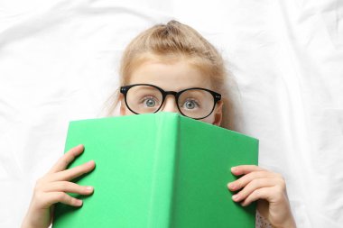Küçük kız yatakta yatarken kitap ile