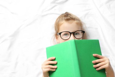Küçük kız yatakta yatarken kitap ile