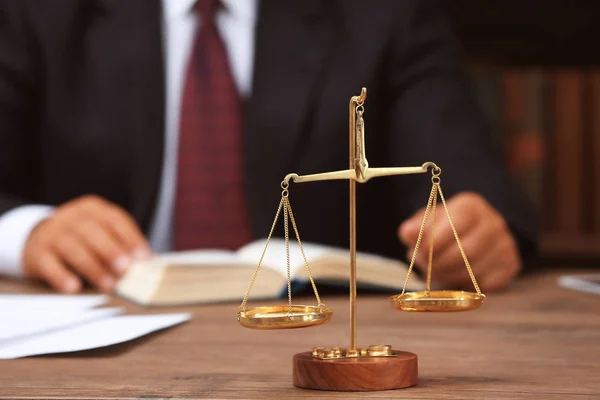 Масштаби справедливості на дерев'яному столі і юрист на фоні — стокове фото