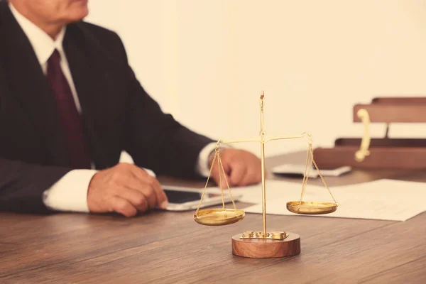 Escalas de justiça na mesa de madeira e advogado masculino em segundo plano — Fotografia de Stock