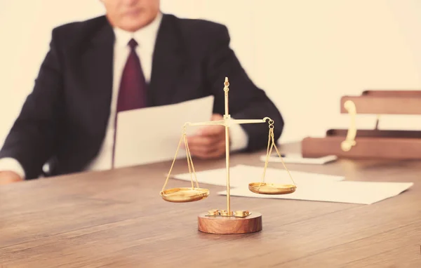 Bilance di giustizia su tavolo di legno e avvocato di sesso maschile su sfondo — Foto Stock