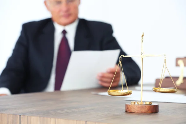 Κλίμακες της δικαιοσύνης σχετικά με ξύλινο τραπέζι και αρσενικό δικηγόρος σε φόντο — Φωτογραφία Αρχείου