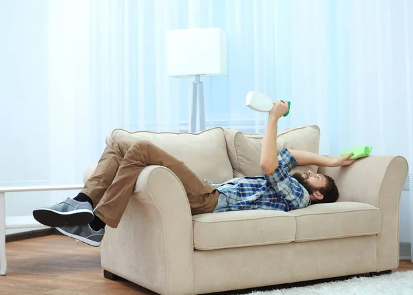 Jeune homme drôle couché sur le canapé avec serviette et détergent — Photo