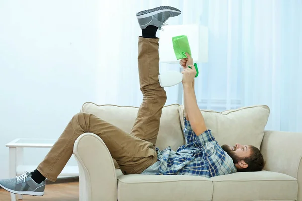 Jeune homme drôle couché sur le canapé avec serviette et détergent — Photo