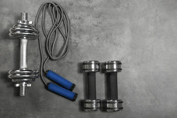 Dumbbells and skipping rope on grey textured background — Stock Photo, Image