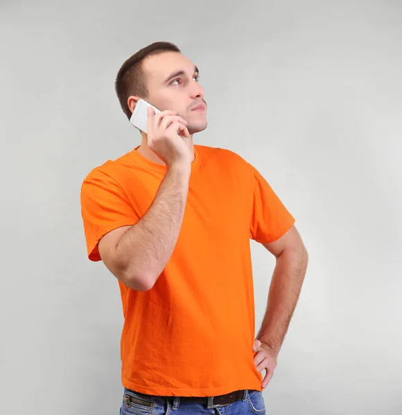 Schöner Mann, der mit dem Handy auf hellem Hintergrund spricht — Stockfoto