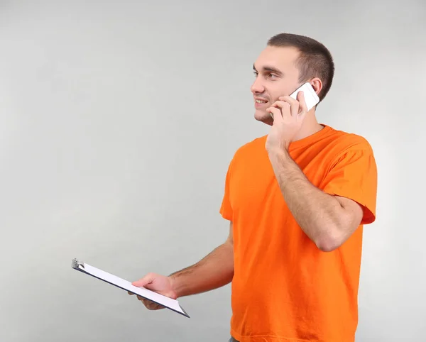 Handsome man holding clipboard while talking by mobile phone, on light background — Stock Photo, Image