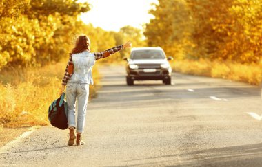 Sırt çantalı genç bir kadın yolda otostop çekiyor.