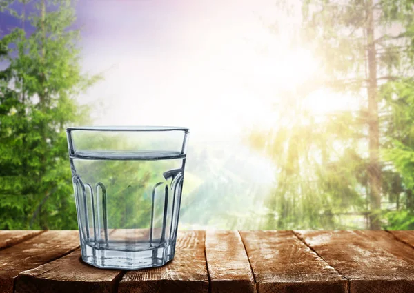 Стакан чистой воды на деревянном столе на фоне природы — стоковое фото
