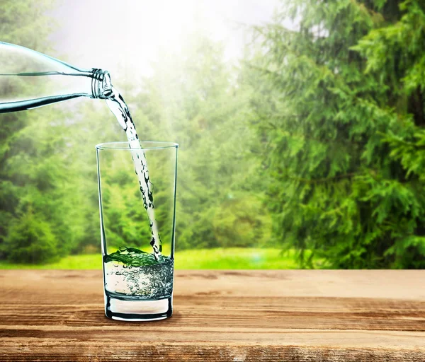 Пролить чистую воду в стекло на природном фоне — стоковое фото
