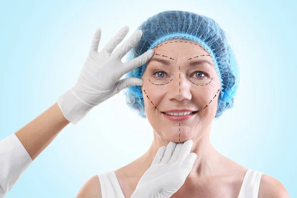 Chirurg untersucht weibliches Gesicht vor blauem Hintergrund. Konzept der plastischen Chirurgie — Stockfoto