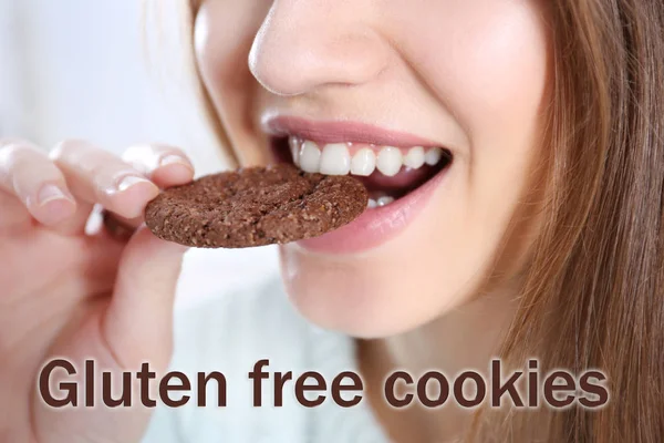 Junge Frau beim Keksessen. Text glutenfreie Cookies auf Hintergrund — Stockfoto
