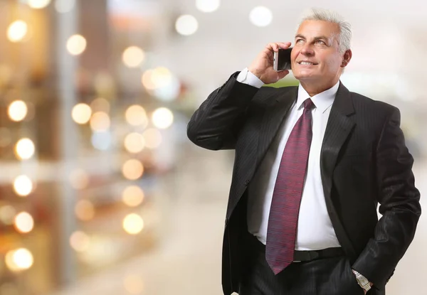 Mature man talking on phone against shopping mall background. Wholesale and logistics concept — Stock Photo, Image