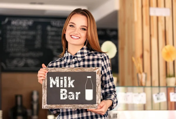 Jovem segurando pequena lousa com texto LEITE BAR no fundo interior — Fotografia de Stock