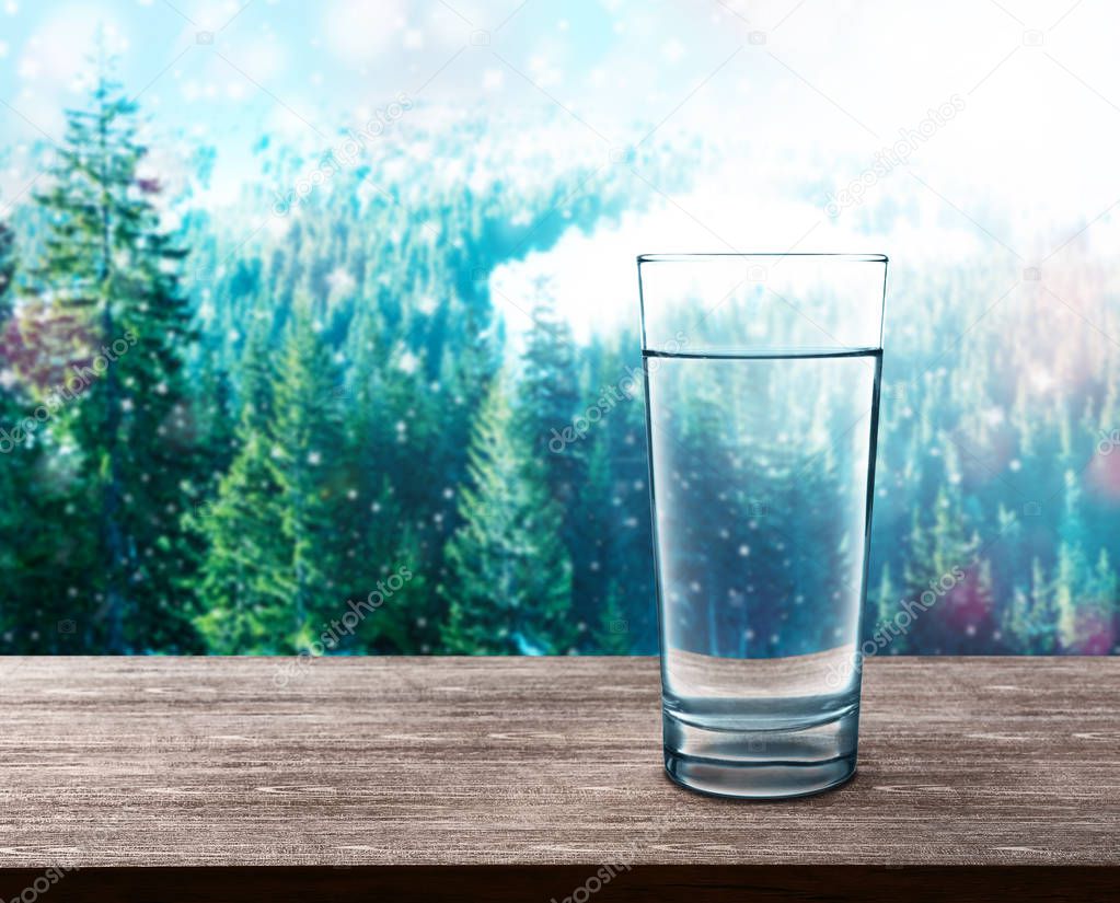 Glass of clear water on wooden table against nature background