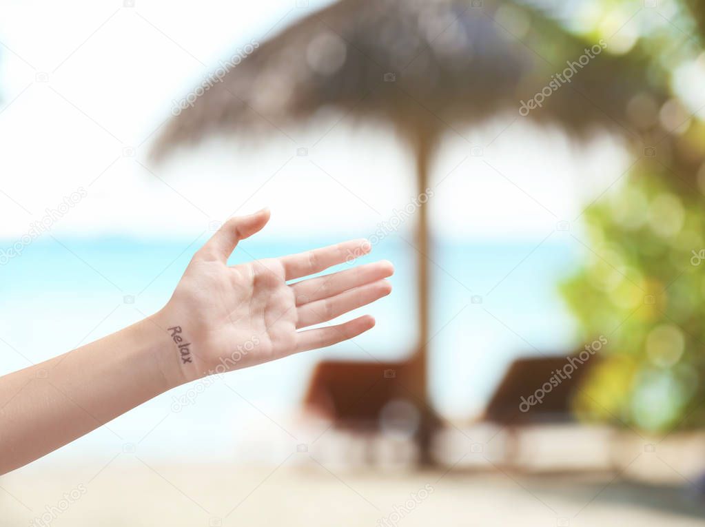 Female hand with word RELAX on ocean beach background