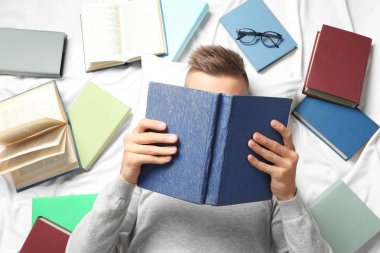 Genç adam yatakta yatarken kitap okuma