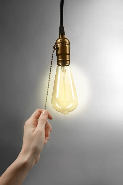 Female hand turning on light bulb on  grey background — Stock Photo, Image