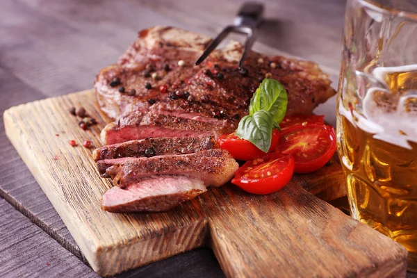 Gegrilde steak met tomaten op de snijplank en mok van bier — Stockfoto