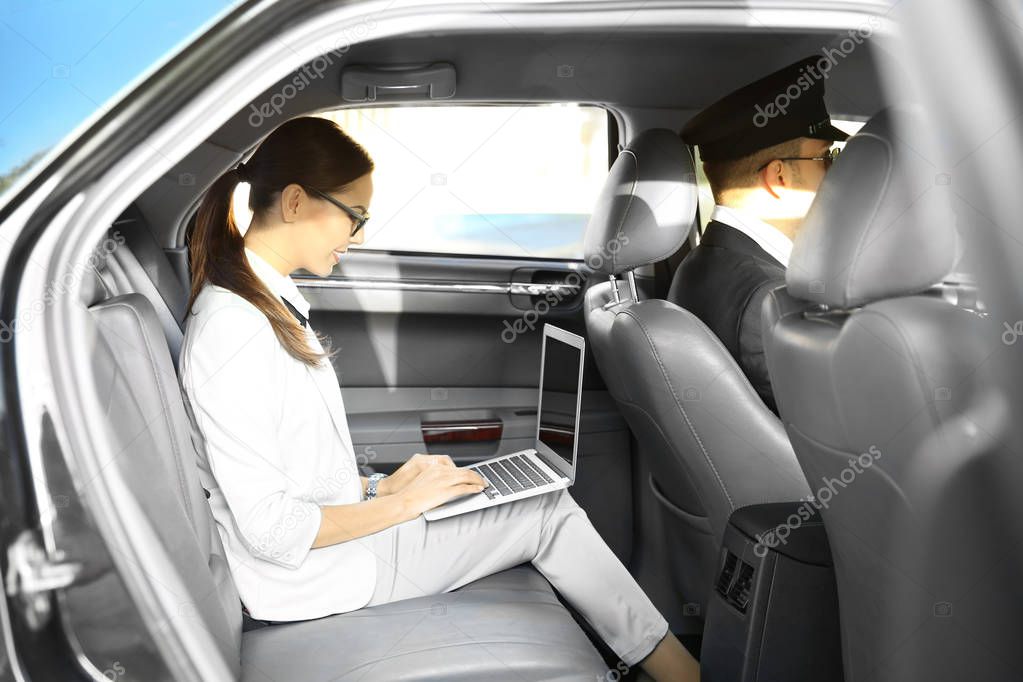 Businesswoman with laptop riding a car with chauffeur