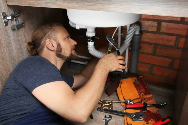 Handsome plumber repairing sink pipes in kitchen — Stock Photo, Image