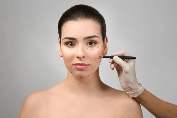 Surgeon drawing marks on female face against gray background. Plastic surgery concept
