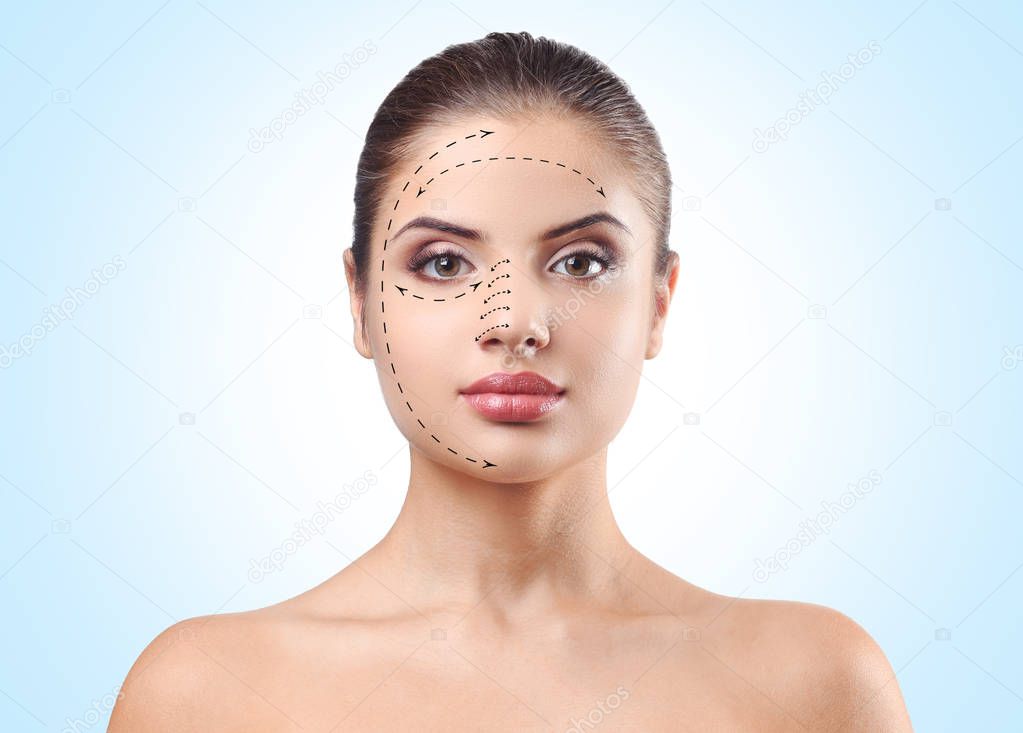 Young woman with marks on face against blue background. Plastic surgery concept