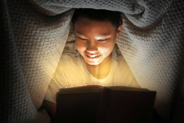 Sevimli çocuk geceleri battaniye altında kitap okuma. Sihirli ışık kitaptan geliyor.