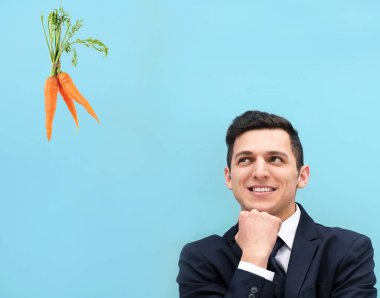 Motivasyon ve hedef kavramı. Genç adam havuç, mavi arka plan arıyorum