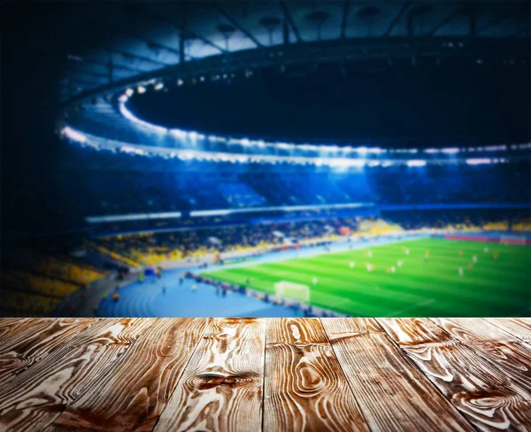 Wooden table against football stadium — Stock Photo, Image
