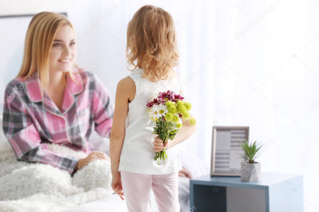 Little girl hiding bouquet of flowers for her mother behind back. Mother's day concept