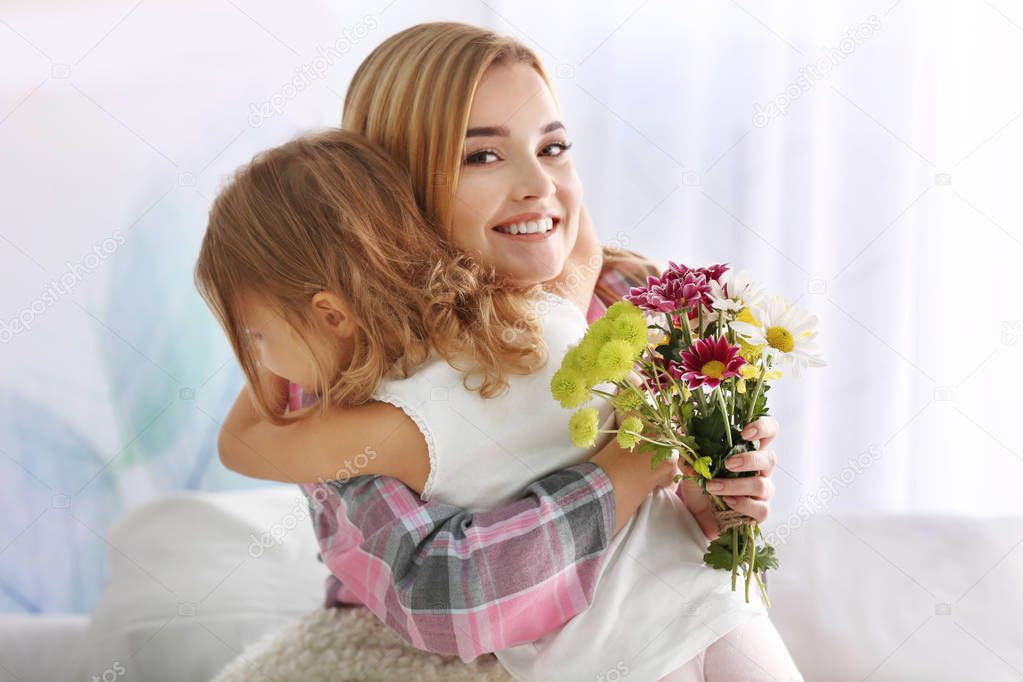 Beautiful young woman hugging her daughter at home. Mother's day concept