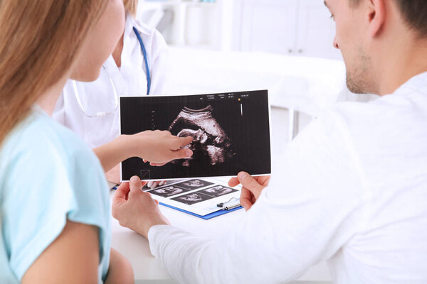 Консультация гинеколога. Врач показывает ультразвуковое сканирование ребенка паре
