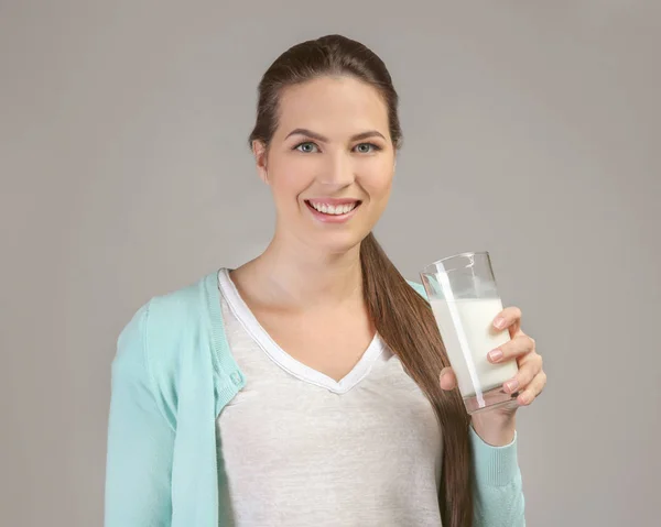 灰色の背景にミルクのガラスを持つ若い魅力的な女性 — ストック写真