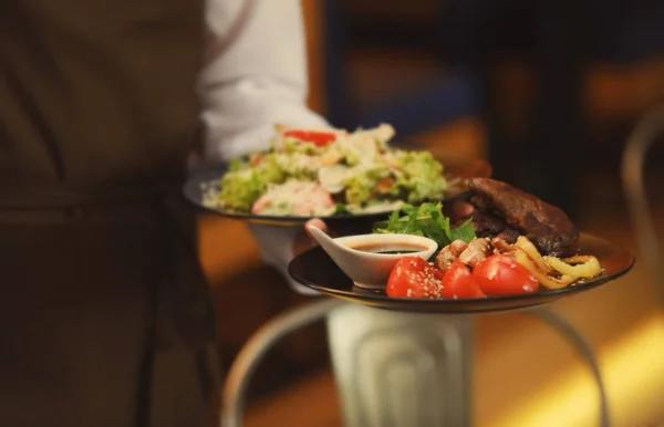 Kellner hält Teller mit leckeren Gerichten — Stockfoto