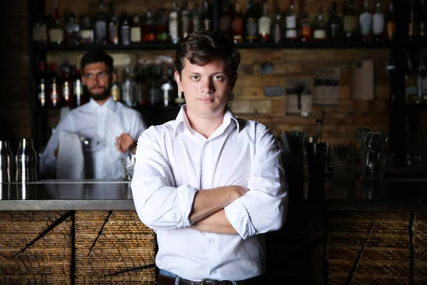 Man with crossed arms standing near wooden bar counter