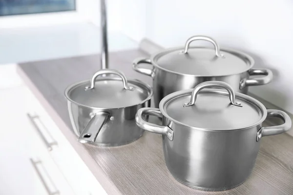 Stainless saucepans on kitchen table — Stock Photo, Image