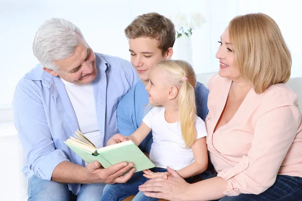 Nette Kinder mit Großeltern lesen Buch, während sie auf dem Sofa im Wohnzimmer sitzen — Stockfoto