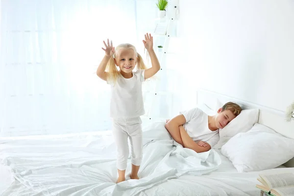 可爱的小女孩在床上跳 而她的哥哥正在睡觉 — 图库照片