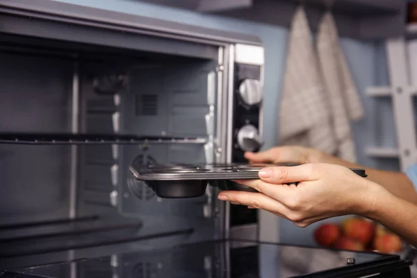 Mujer poniendo bandeja de magdalenas en el horno — Foto de Stock