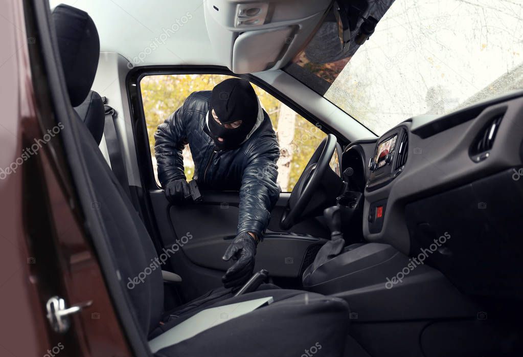 Thief in mask stealing laptop from a car