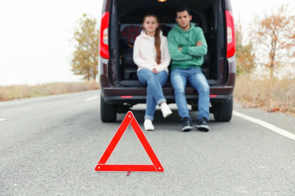 Traffic warning sign on road with car and couple on background