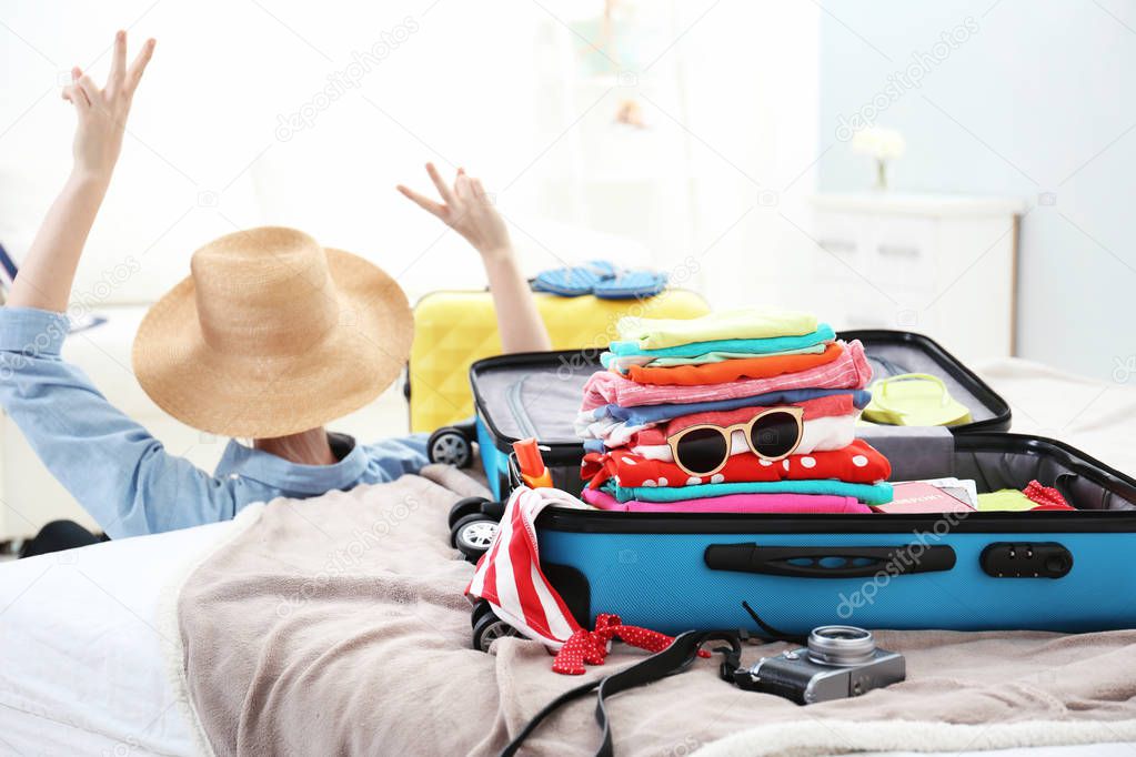 Opened traveler case with clothes and happy woman on background