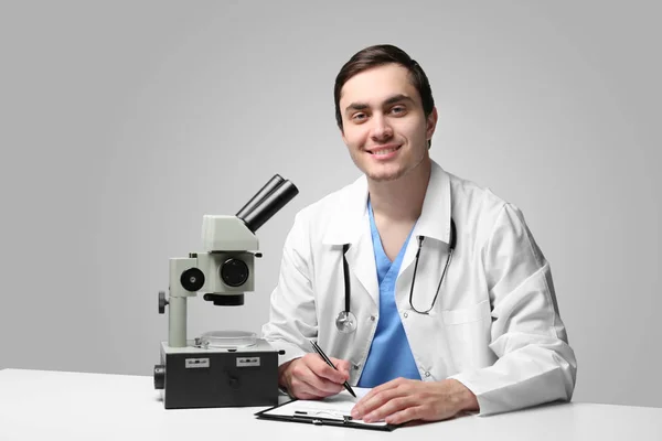 Jovem Médico Trabalhando Com Microscópio Mesa Fundo Claro — Fotografia de Stock