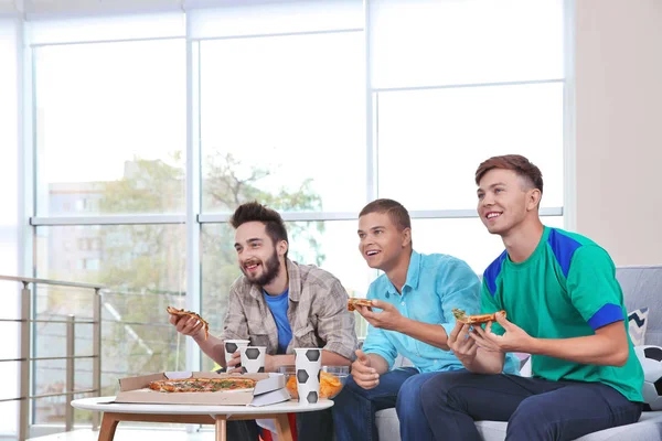 Futbol hayranları oyunu odasında izlerken pizza ile