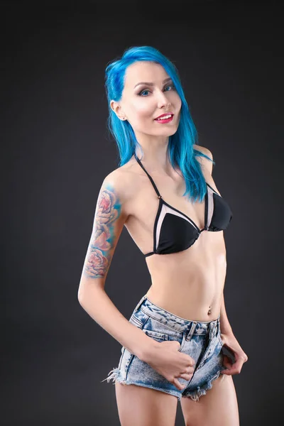 Belle jeune femme avec des cheveux de couleur élégante et tatouage sur fond sombre — Photo