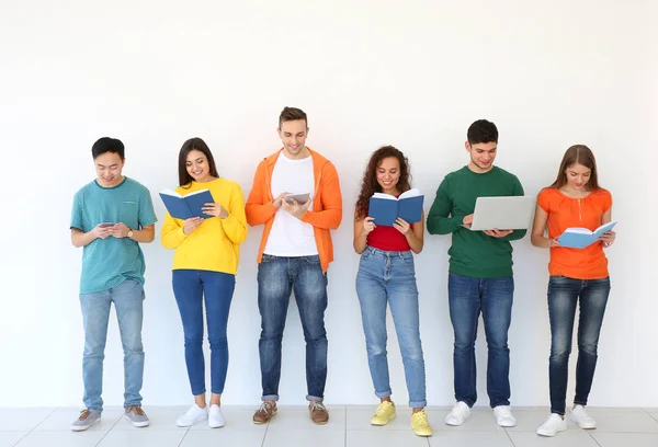 People with books and gadgets standing near light wall