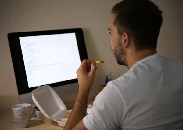 Hombre comiendo bocadillos mientras trabaja con la computadora —  Fotos de Stock