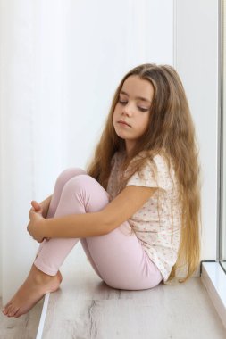 Pencere kenarında oturan küçük üzgün kız